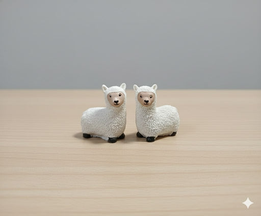 Pair of white miniature sheep figurines on a wooden surface.