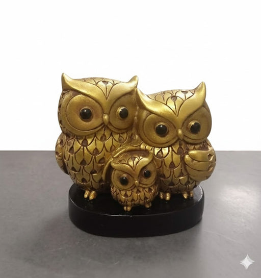 A metallic gold owl family showpiece depicting two adult owls and one baby owl, standing on a dark wooden base.