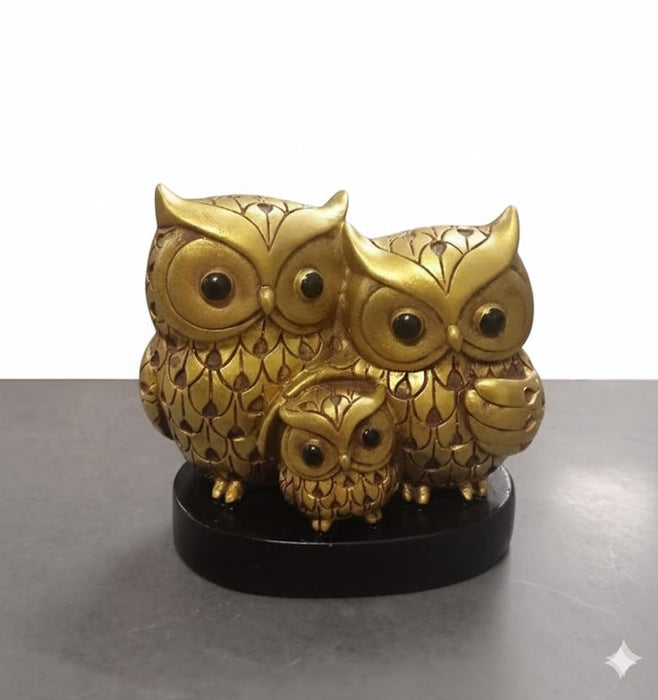 A metallic gold owl family showpiece depicting two adult owls and one baby owl, standing on a dark wooden base.