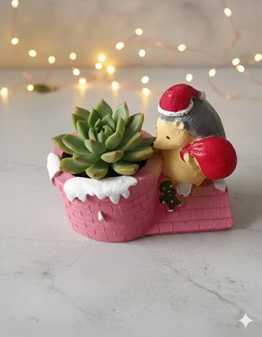 A cute hedgehog figurine wearing a Santa hat and holding a red sack, perched on a pink chimney-shaped planter/pot, with white snow accents.