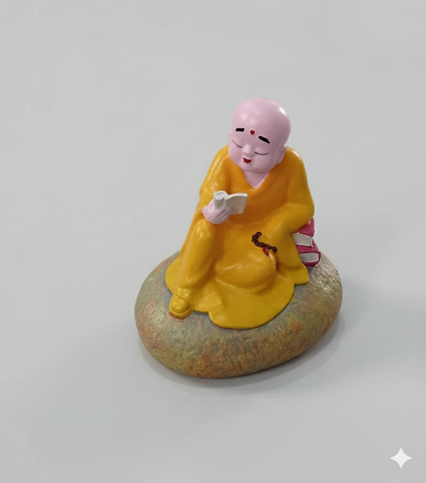 Small orange-robed monk figurine reading a book, peaceful Zen Buddha statue for home office desk and bookshelf decor.