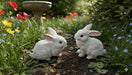Two white ceramic rabbit figurines with pink ears and red eyes sitting on a grey floor.