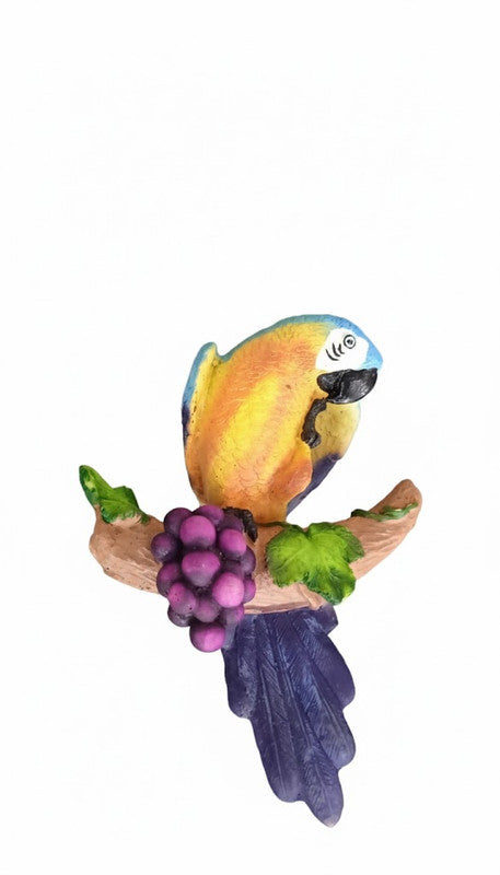 Colorful ceramic or resin figurine of a blue and gold macaw parrot perched on a brown branch with a bunch of purple grapes.