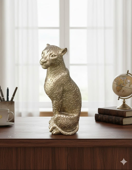 Gold metallic leopard statue/figurine with a textured ring pattern, sitting on a dark wooden desk in front of a bright window, next to a vintage globe and books.