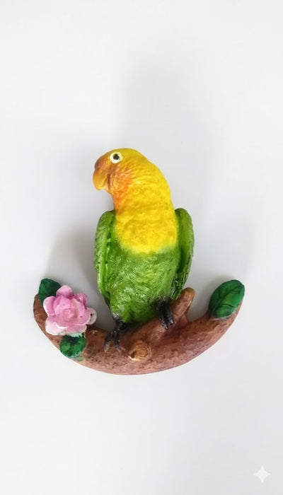 Hand-painted resin figurine of a yellow-headed, green parrot perched on a brown branch with a pink flower.