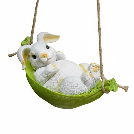 A small white resin bunny figurine with yellow accents, relaxing on its back in a vibrant green fabric hammock swing suspended by rope.