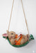 Decorative figurine of a bunny and a mouse reading a book together while relaxing in a green hammock, hanging by twine rope against a white wall.