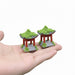 "Pair of miniature Chinese-style garden pavilions or pagodas with red pillars, grey base, and green flocking moss on the roof and around the base, held in the palm of a hand."