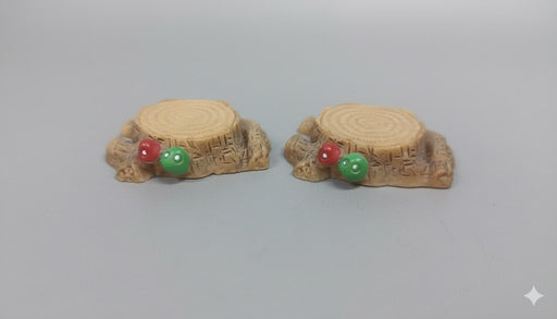Two miniature resin tree stumps with tiny red and green mushrooms on a gray background.