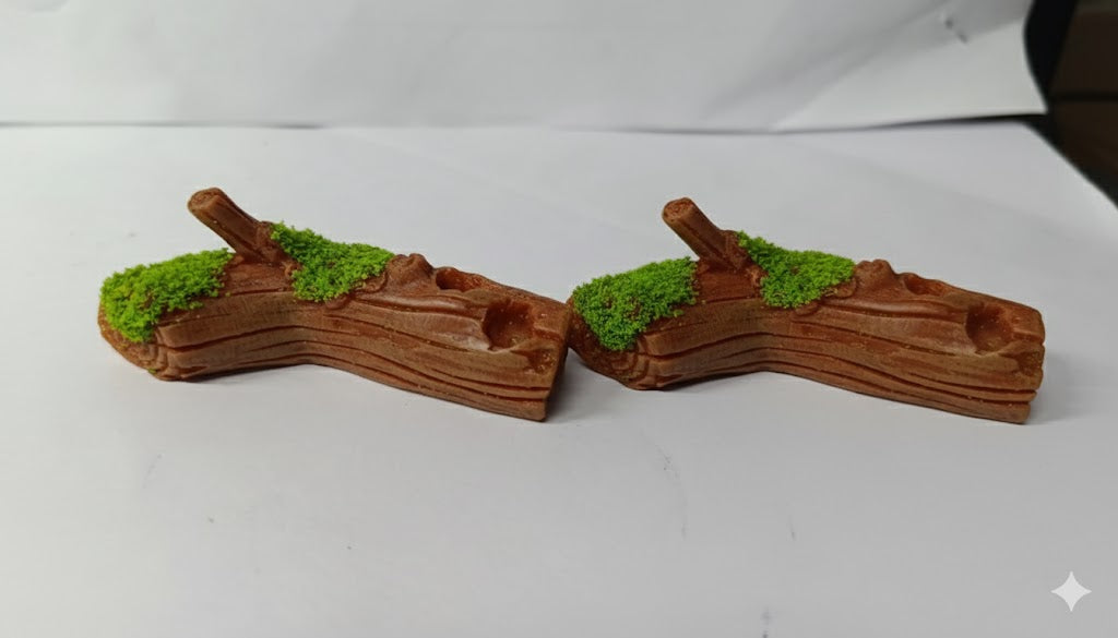 Two small, synthetic, brown resin log decorations, featuring detailed wood grain texture and patches of vibrant green artificial moss on the upper surface.