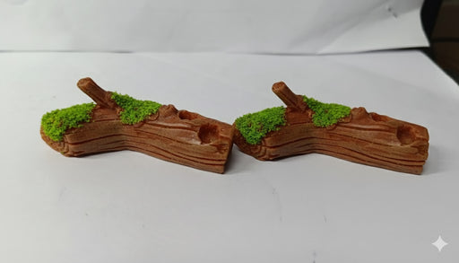 Two small, synthetic, brown resin log decorations, featuring detailed wood grain texture and patches of vibrant green artificial moss on the upper surface.