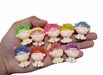 A hand holding nine small, colorful resin baby doll figurines with translucent hair in shades of blue, purple, yellow, pink, green, and red,
