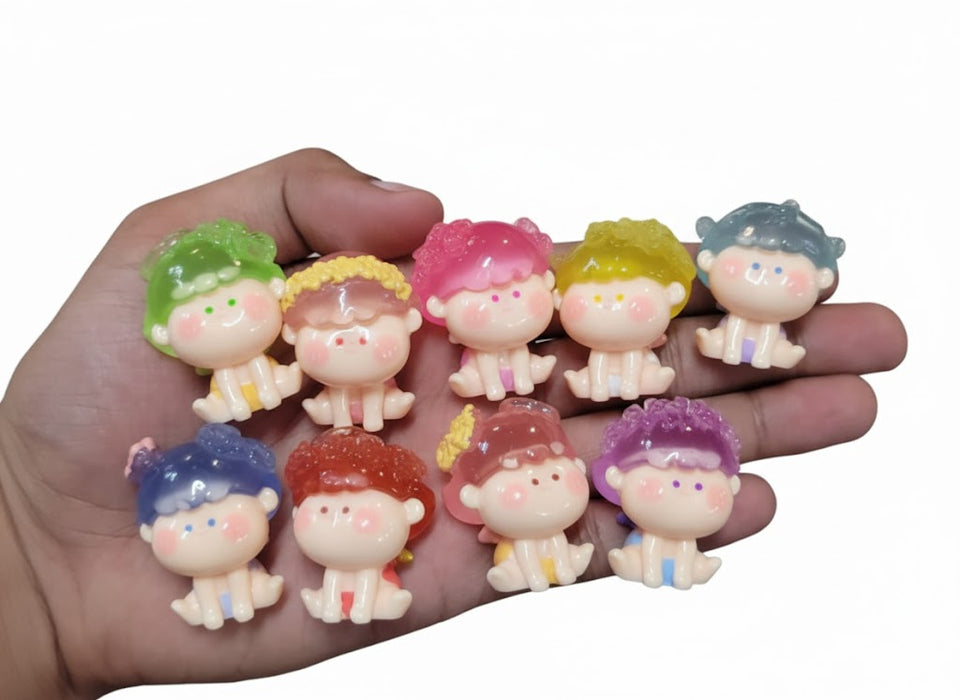 A hand holding nine small, colorful resin baby doll figurines with translucent hair in shades of blue, purple, yellow, pink, green, and red,