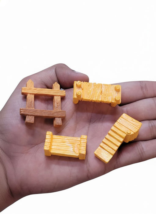 A hand holding four miniature wooden-look accessories: one dark brown picket fence, two light orange wooden benches, and one light orange set of stairs