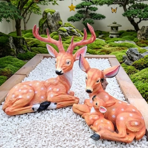 Realistic 2-piece Sika deer garden statue set featuring a majestic spotted buck and a mother doe with baby fawn resting on white decorative stones in a lush green Zen garden.