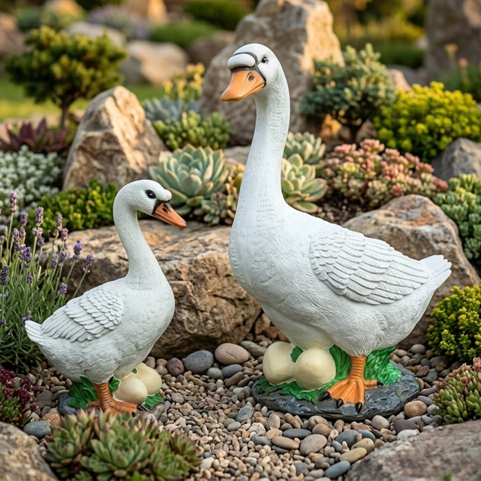 White goose and duck garden statues with eggs, placed in a landscaped rock garden featuring succulents, lavender, and smooth grey pebbles.