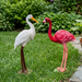 "A pair of life-sized garden statues featuring a white crane with an orange beak and a vibrant pink flamingo standing on artificial green grass in an outdoor decor display."