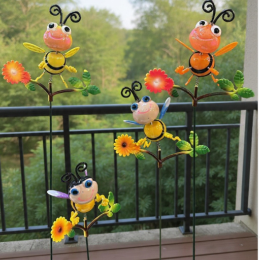 Hand-painted metal bee and butterfly garden stakes placed in a flower bed with soil, lavender, and pink flowers in a sunny backyard setting.