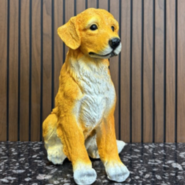 Light orange puppy dog statue sitting on a stone path in a lush garden with flowers and a water fountain