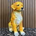 Light orange puppy dog statue sitting on a stone path in a lush garden with flowers and a water fountain