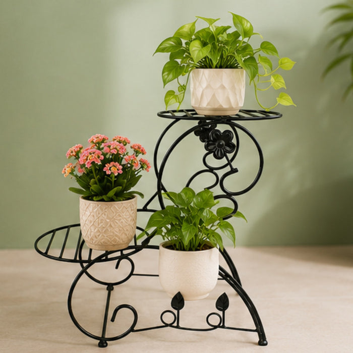 Black metal multi-tier plant stand featuring decorative scrollwork and floral accents on a plain white background