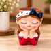 4-inch polyresin cute girl face planter in a red dress with a white polka-dot bow headband, placed on a wooden table (plant not included).