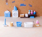 A 15-piece miniature pastel blue, white, and pink laundry and bathroom set arranged on a light tabletop, including a washing machine, sink vanity, bathtub, laundry baskets, cleaning supplies, and bathroom accessories.
