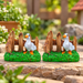 Set of two miniature white duck figurines standing on green grass with a rustic wooden fence background