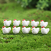 A small glossy white miniature hen figurine with a red comb and yellow beak standing on a green grass landscape