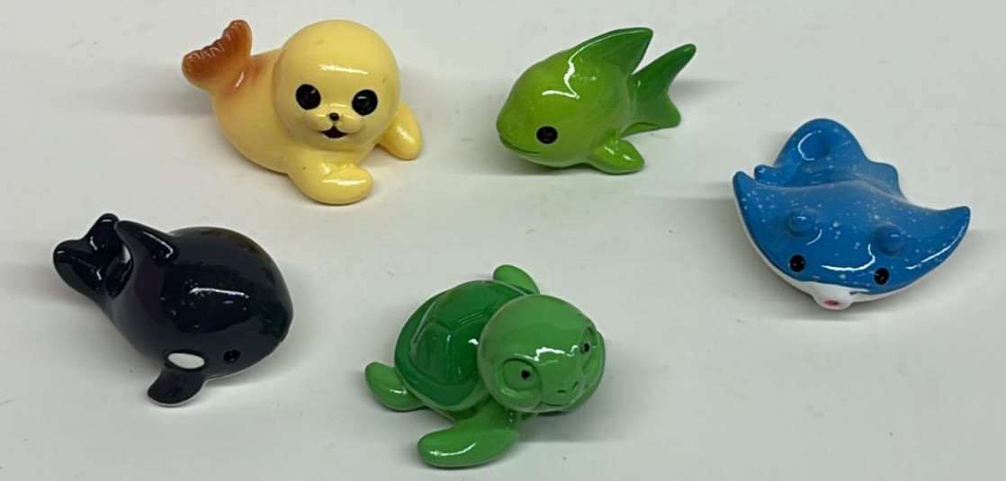 A set of 5 cute miniature ocean animal figurines including a yellow seal, green sea turtle, black orca, green fish, and speckled blue stingray