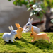 Set of 4 miniature white and orange rabbit figurines arranged on green moss in a garden setting.