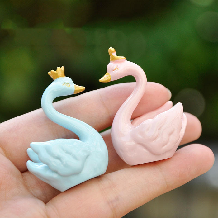 Set of two cute pastel blue and pink ceramic swan figurines with gold crowns and beaks displayed on a wooden surface.