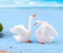 Set of 2 cute white miniature swan figurines with detailed wings displayed side by side against a blue background