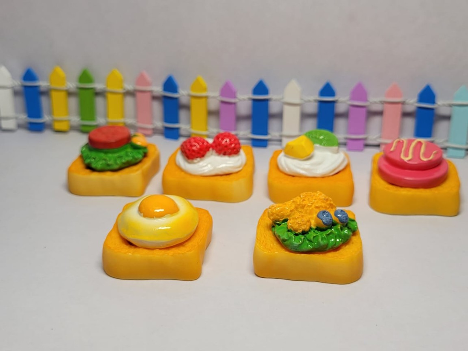 Set of 6 assorted miniature toast resin pieces featuring various toppings like fried egg and strawberries arranged against a colorful mini fence background.