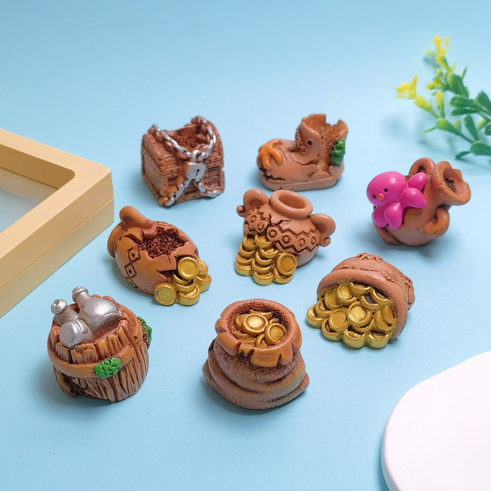 Set of 8 miniature nautical treasure figurines arranged on a light blue background, including a chained chest, sunken boot, pink octopus in a jar, pots of gold coins, sacks of gold, and a barrel with silver bottles.